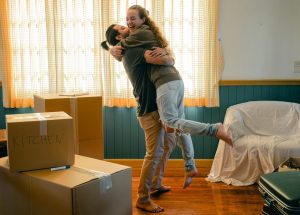 Happy couple hugging in their new living room surrounded by moving boxes, representing the wide scope of mortgage options available through a broker.