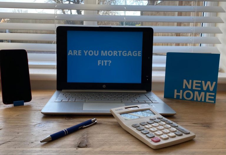 Laptop screen displaying “Are you mortgage fit?” with a pen and calculator on the table.