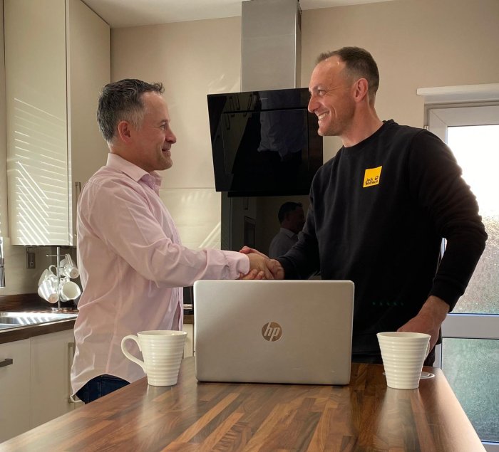 Mortgage advisor shaking hands with a client over a laptop during a home consultation, with two cups of tea on the table.